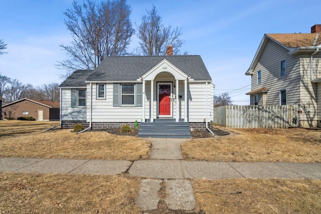 bungalow-style home with a shingled roof, a chimney, and fence