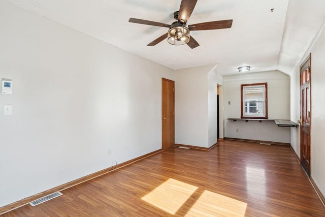 empty room featuring ceiling fan, visible vents, baseboards, and wood finished floors