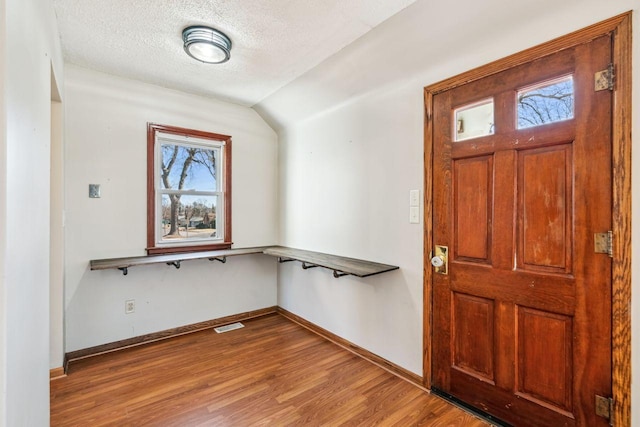 foyer entrance with visible vents, lofted ceiling, a textured ceiling, wood finished floors, and baseboards