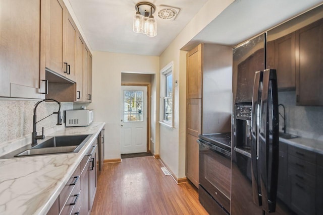 kitchen featuring wood finished floors, light stone countertops, a sink, decorative backsplash, and black appliances