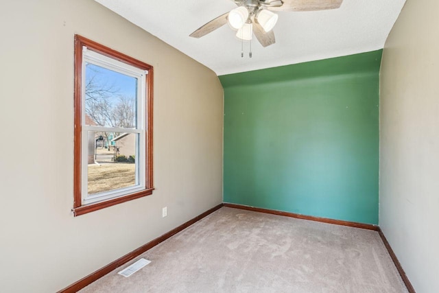 empty room with a ceiling fan, light colored carpet, visible vents, and baseboards