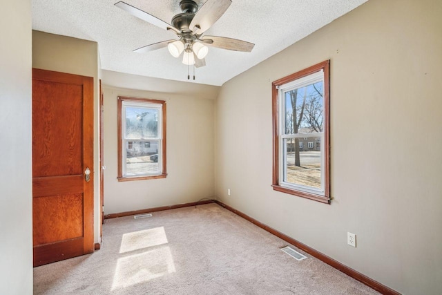 empty room featuring baseboards, visible vents, ceiling fan, a textured ceiling, and light carpet