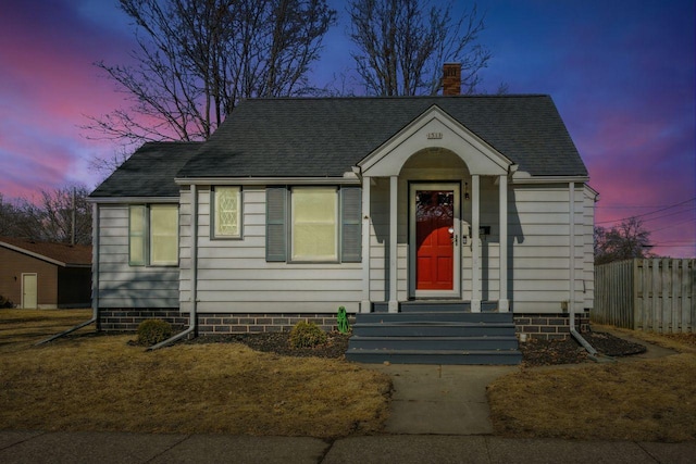 bungalow-style home with a shingled roof, a chimney, and fence