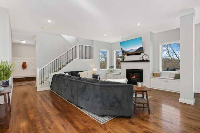 living area with a large fireplace, stairway, a wealth of natural light, and wood finished floors