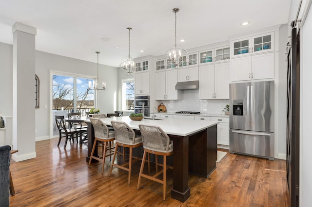 kitchen featuring stainless steel appliances, a chandelier, under cabinet range hood, and tasteful backsplash