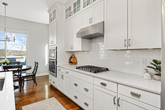 kitchen with under cabinet range hood, dark wood-type flooring, light countertops, appliances with stainless steel finishes, and decorative backsplash