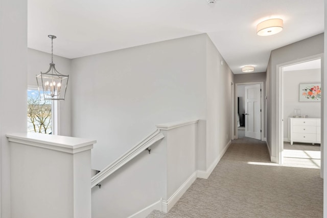 hall with a notable chandelier, carpet flooring, an upstairs landing, and baseboards