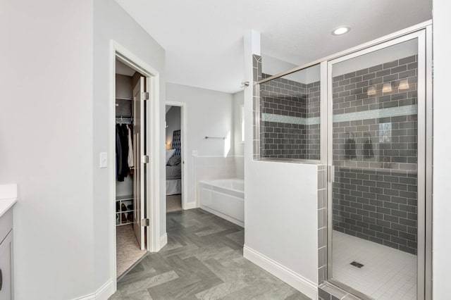 full bathroom with vanity, baseboards, a spacious closet, a bath, and a stall shower