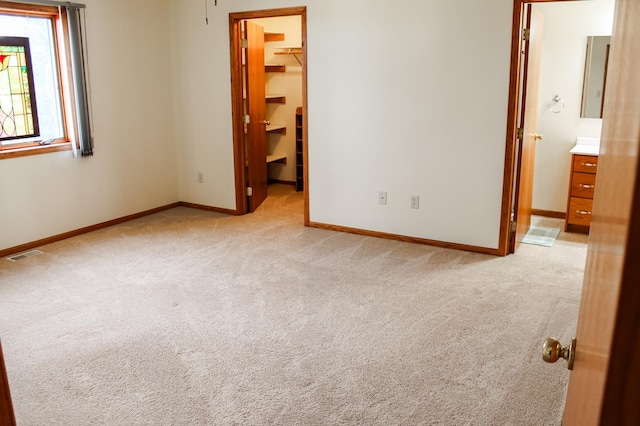 unfurnished bedroom featuring a spacious closet, visible vents, baseboards, light colored carpet, and a closet