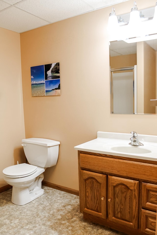 bathroom featuring vanity, baseboards, a drop ceiling, an enclosed shower, and toilet