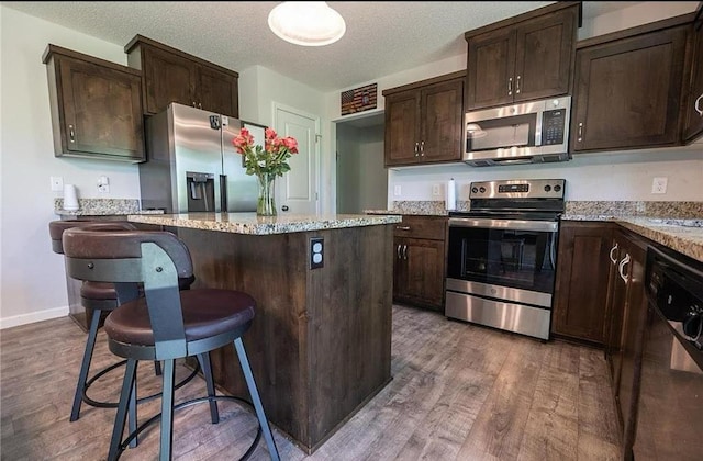 kitchen with a breakfast bar, light wood-style floors, dark brown cabinets, appliances with stainless steel finishes, and a center island