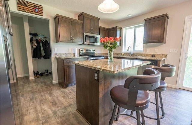 kitchen with a breakfast bar area, wood finished floors, a center island, stainless steel appliances, and a sink