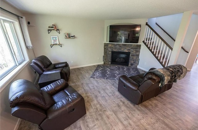 living room featuring baseboards, stairway, wood finished floors, a textured ceiling, and a stone fireplace