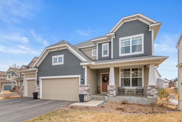 craftsman-style home with a porch, aphalt driveway, a garage, stone siding, and roof with shingles