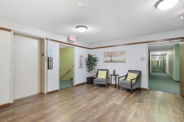 living area featuring baseboards, elevator, a textured ceiling, and wood finished floors