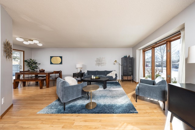 living area featuring a textured ceiling, light wood-type flooring, and baseboards