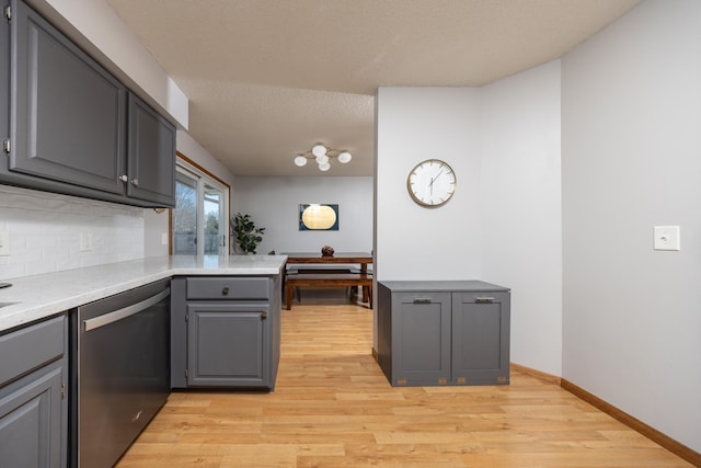 kitchen featuring a peninsula, stainless steel dishwasher, light wood-type flooring, and gray cabinets