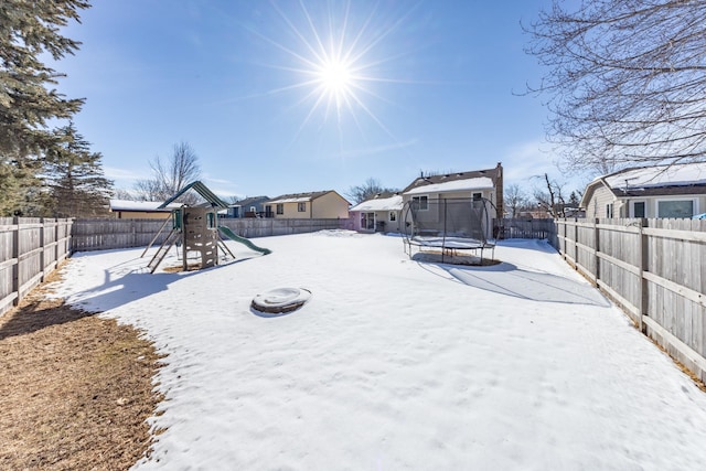 yard layered in snow featuring a trampoline, a playground, and a fenced backyard