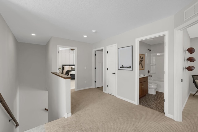 hallway with visible vents, baseboards, carpet, a textured ceiling, and an upstairs landing