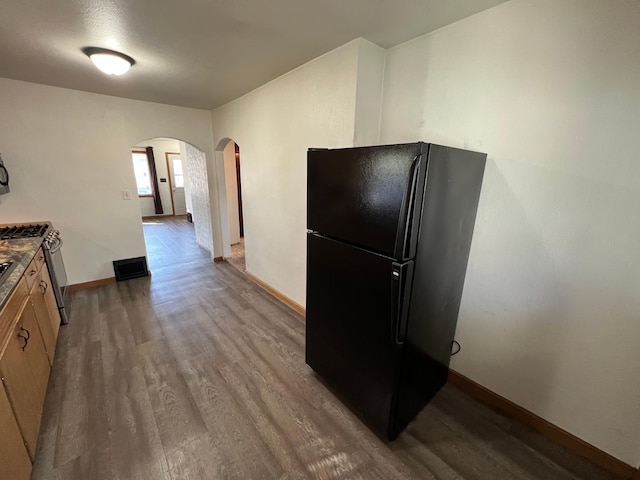 kitchen with visible vents, stainless steel gas stove, freestanding refrigerator, wood finished floors, and arched walkways