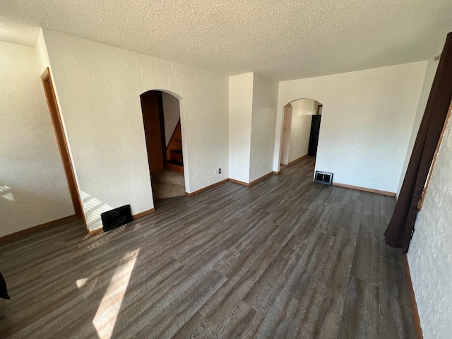 empty room featuring dark wood-style floors, visible vents, arched walkways, stairs, and a textured wall