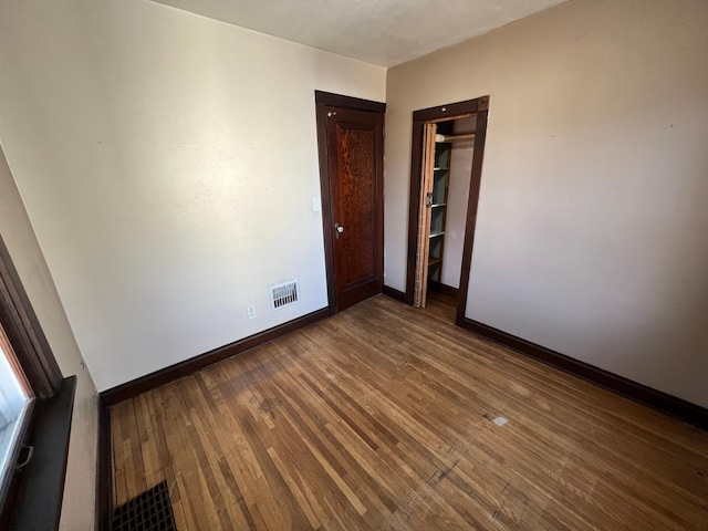 empty room with dark wood-type flooring, baseboards, and visible vents