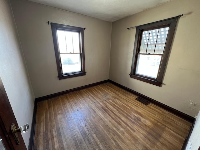 unfurnished room featuring visible vents, baseboards, and wood finished floors