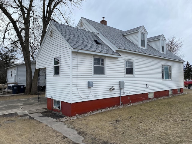 view of home's exterior with roof with shingles, a yard, and a chimney