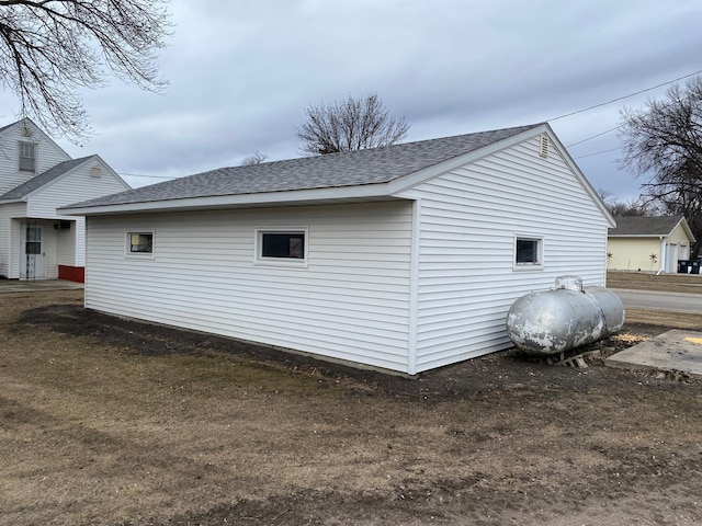 view of side of property featuring a shingled roof and heating fuel