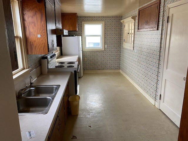 kitchen featuring wallpapered walls, baseboards, electric stove, light countertops, and a sink