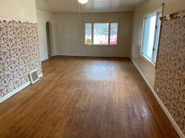 unfurnished room with visible vents, arched walkways, wood finished floors, and a wealth of natural light