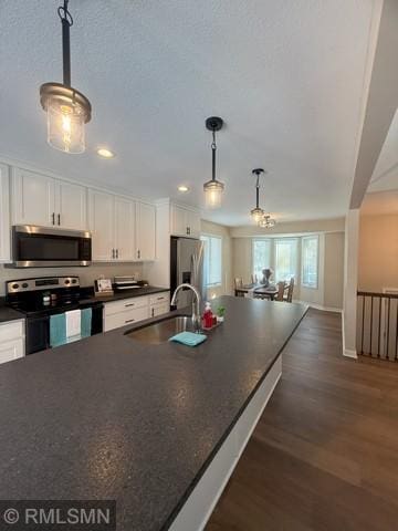 kitchen with stainless steel appliances, dark countertops, dark wood-type flooring, white cabinets, and a sink