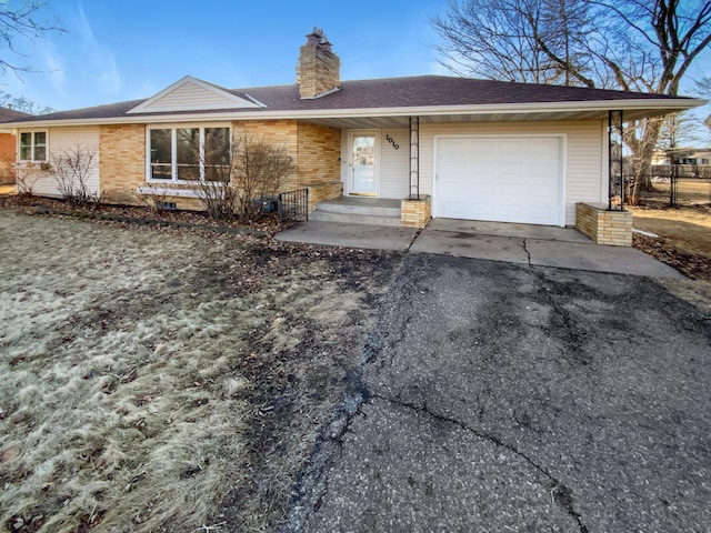 ranch-style home with driveway, an attached garage, a shingled roof, brick siding, and a chimney