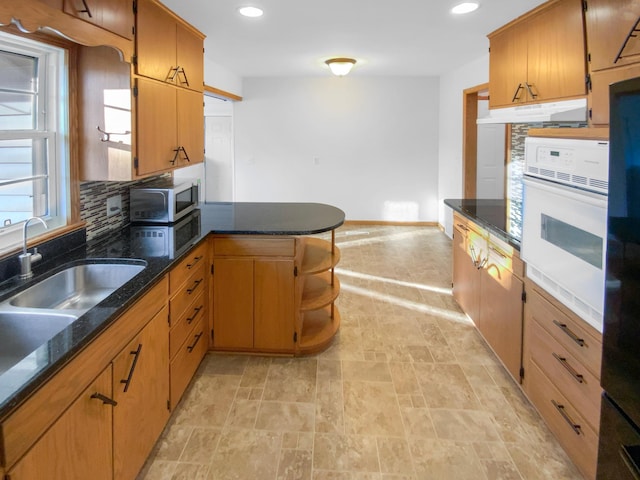 kitchen featuring stainless steel microwave, under cabinet range hood, decorative backsplash, a peninsula, and white oven