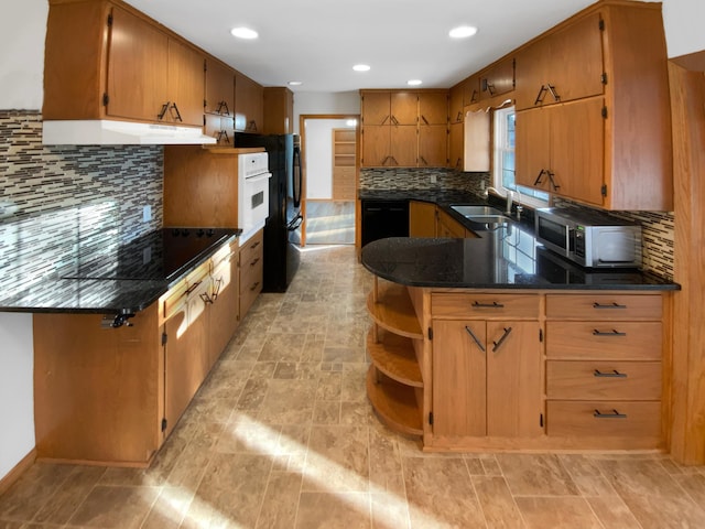 kitchen with backsplash, under cabinet range hood, a peninsula, black appliances, and a sink