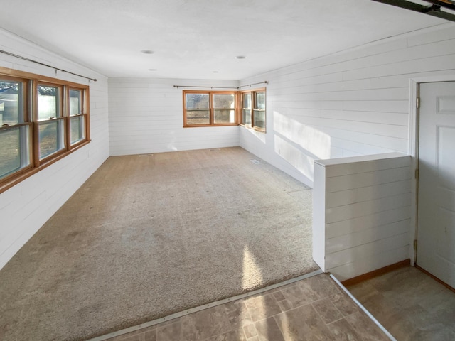 carpeted empty room featuring a healthy amount of sunlight and wood walls