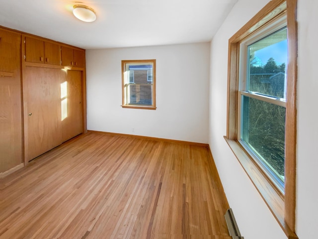 unfurnished bedroom featuring a closet, light wood-type flooring, baseboards, and a baseboard radiator