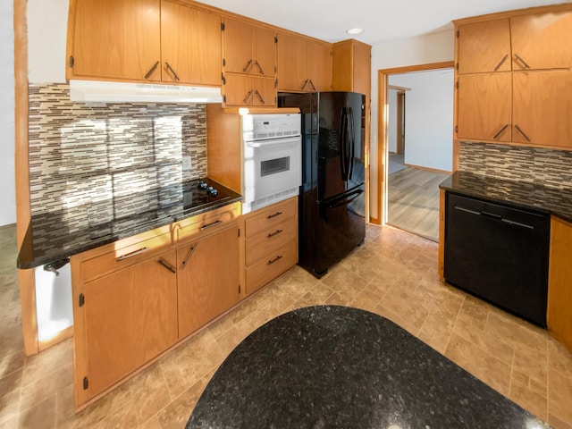 kitchen featuring under cabinet range hood, backsplash, black appliances, and dark stone counters