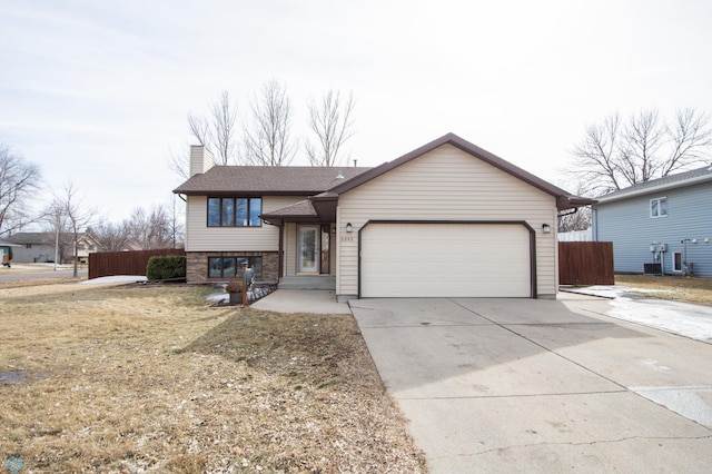 split level home with fence, roof with shingles, an attached garage, a chimney, and concrete driveway