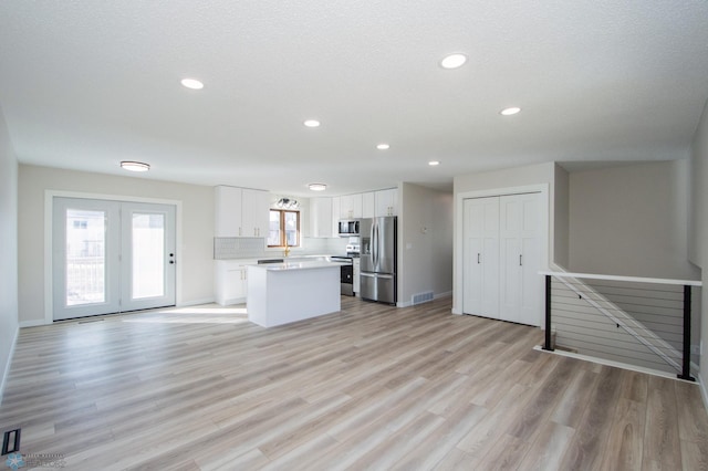 kitchen with light wood finished floors, backsplash, a center island, appliances with stainless steel finishes, and white cabinetry