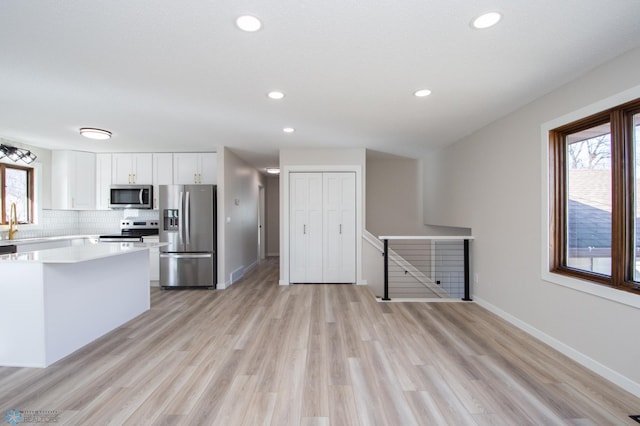 kitchen featuring decorative backsplash, light countertops, white cabinets, appliances with stainless steel finishes, and light wood-type flooring