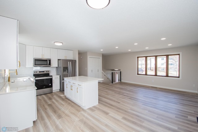 kitchen featuring a center island, decorative backsplash, light wood-style floors, stainless steel appliances, and a sink