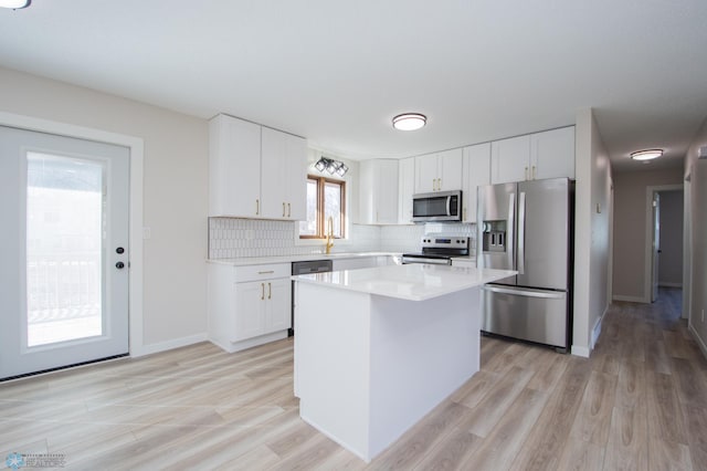 kitchen with a kitchen island, backsplash, appliances with stainless steel finishes, white cabinets, and light countertops