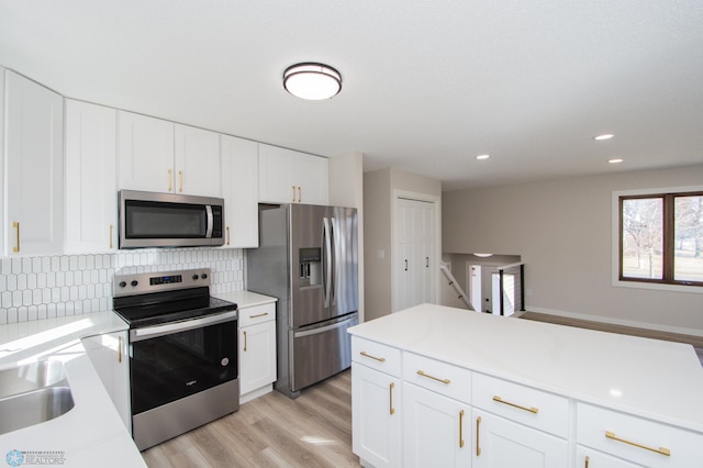 kitchen featuring light wood-type flooring, light countertops, white cabinets, appliances with stainless steel finishes, and tasteful backsplash