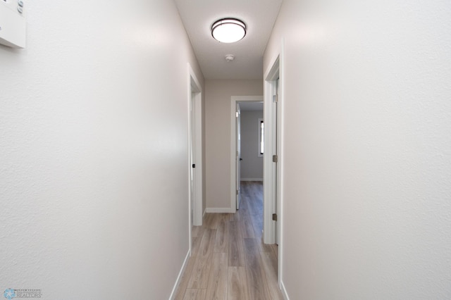 corridor with light wood-type flooring and baseboards