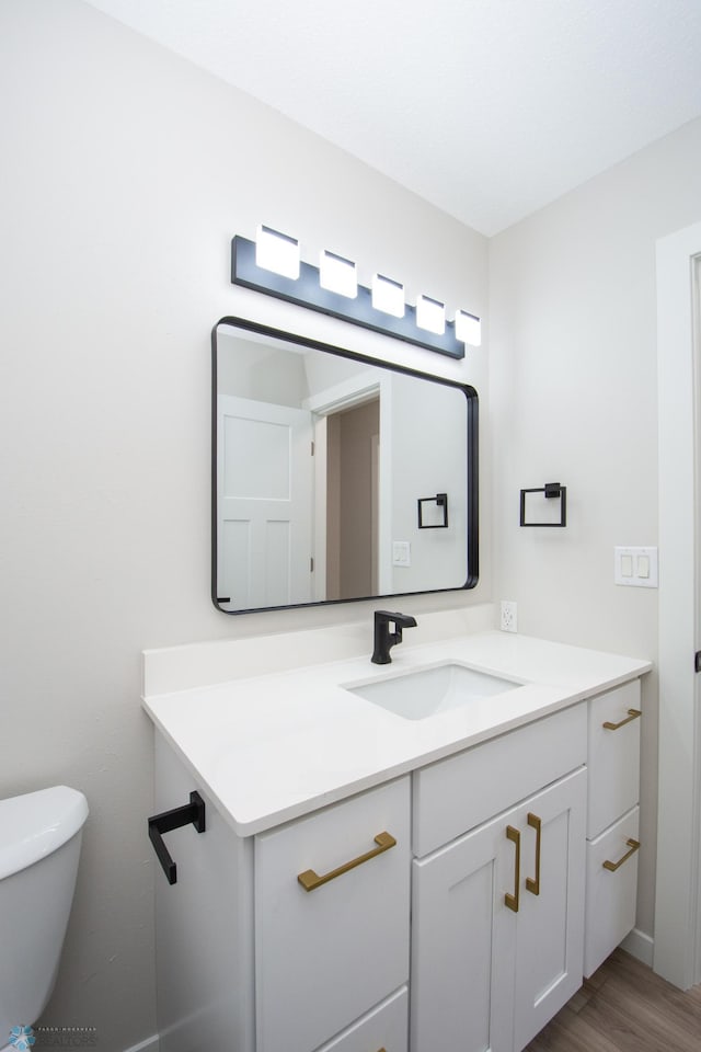 half bath with toilet, wood finished floors, and vanity