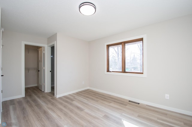 unfurnished bedroom featuring light wood-type flooring, visible vents, baseboards, and a spacious closet