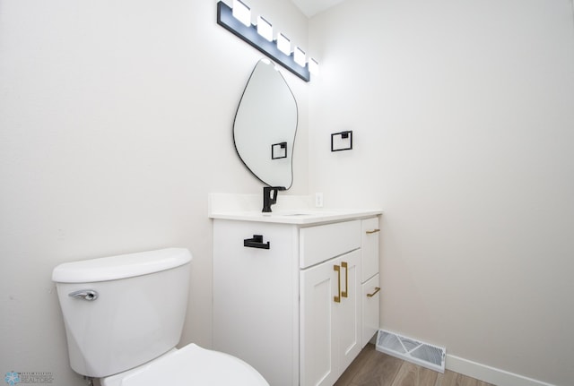 half bathroom with visible vents, baseboards, toilet, wood finished floors, and vanity