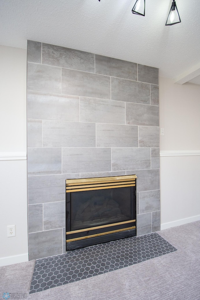 details with a tiled fireplace, carpet, baseboards, and a textured ceiling