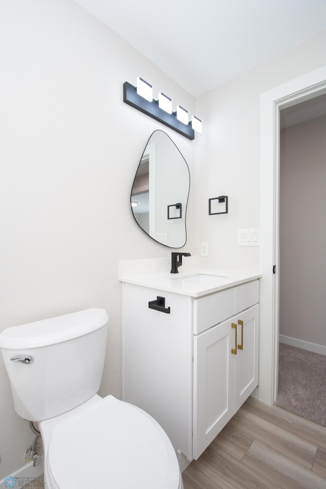 half bath featuring toilet, vanity, baseboards, and wood finished floors